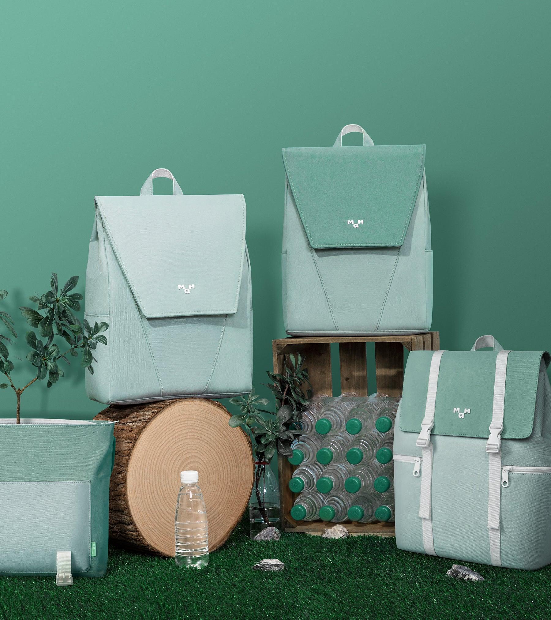 Mint green backpacks and accessories styled with plants, wood, and water bottles on grass