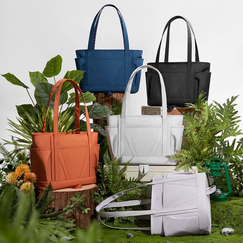 Stylish tote bags in blue, black, white, and orange displayed with lush green plants for a fresh, modern look.