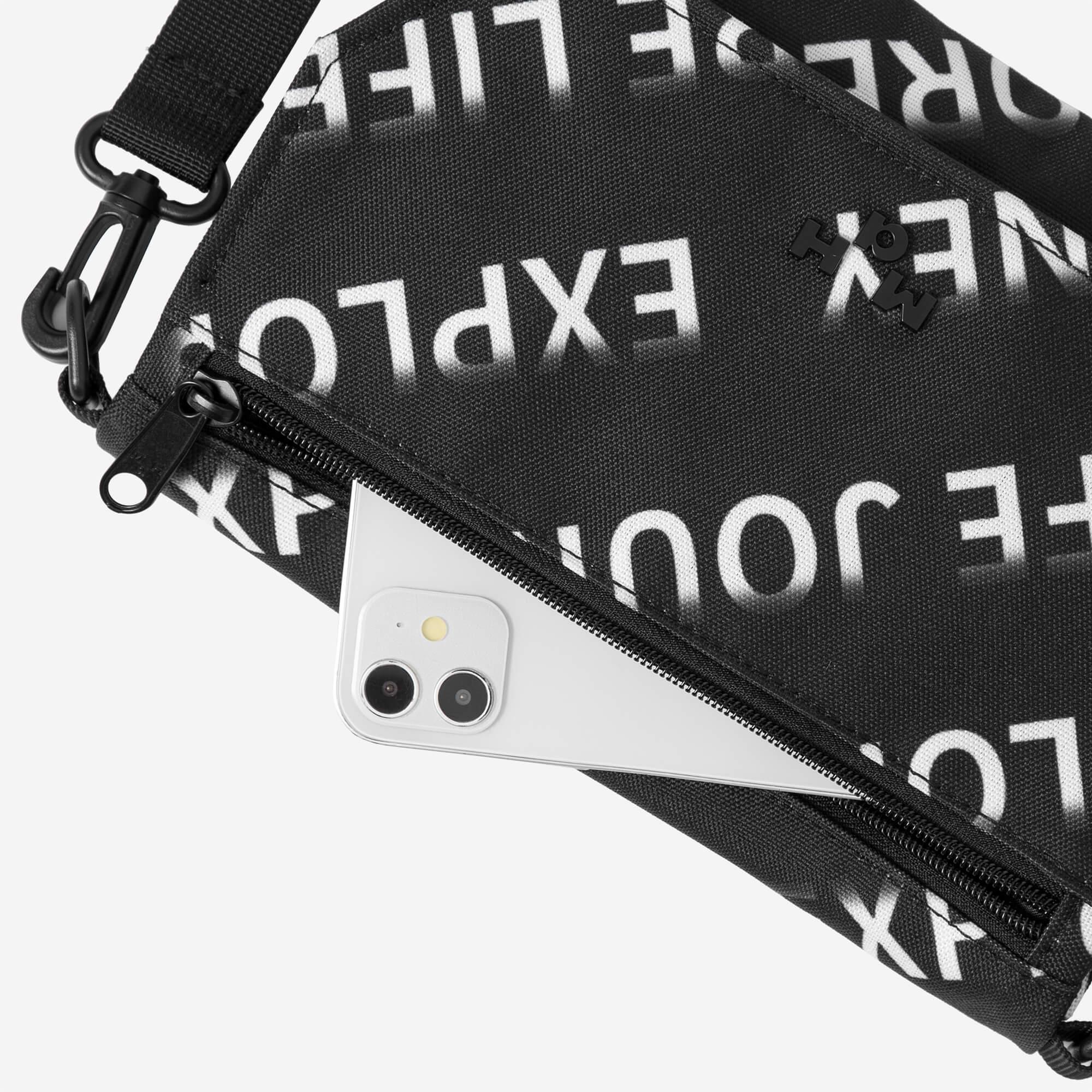 Black crossbody bag with bold white text print, zipper pocket holding smartphone, adjustable strap
