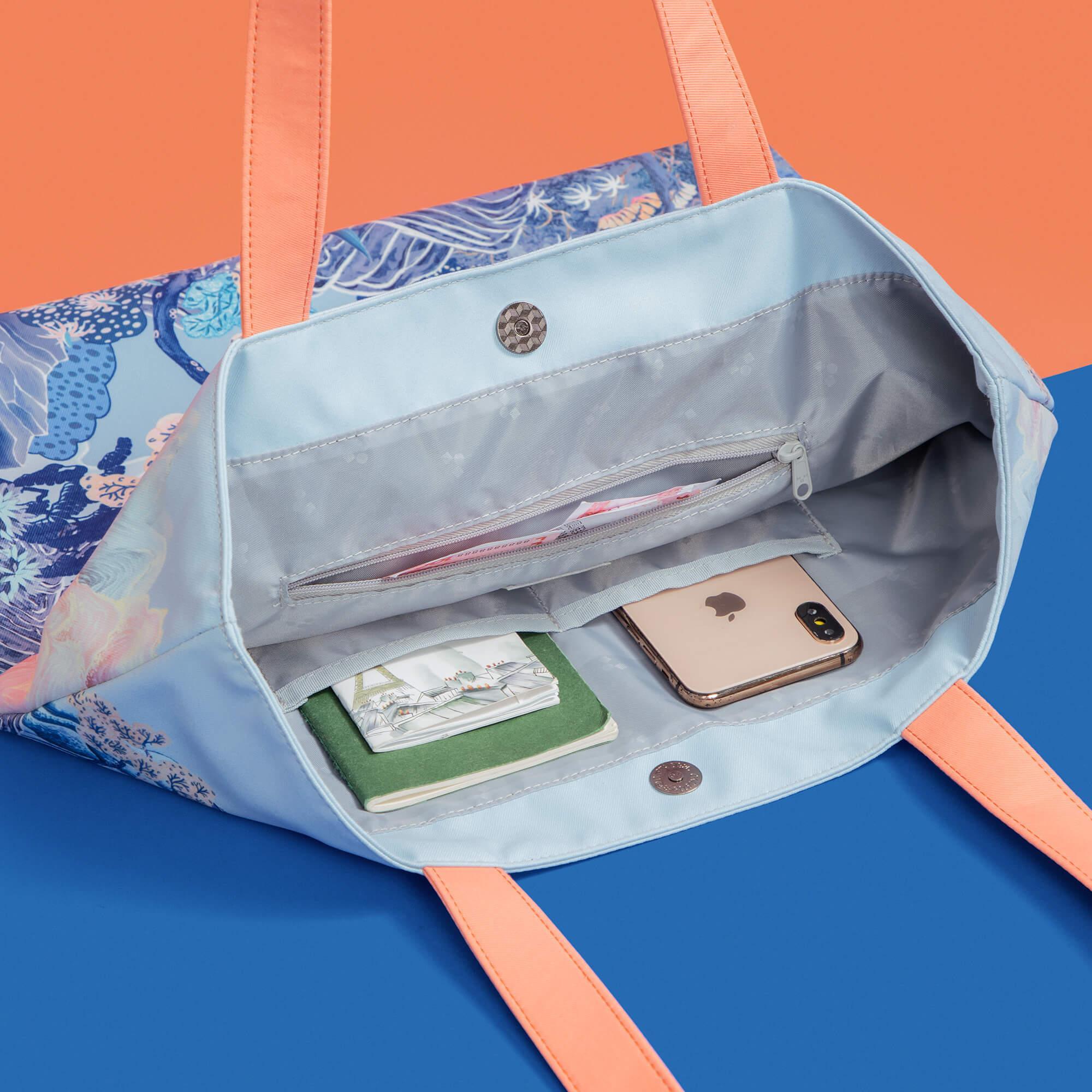 Stylish tote bag with blue floral print, peach straps, and interior pockets holding phone and notebook