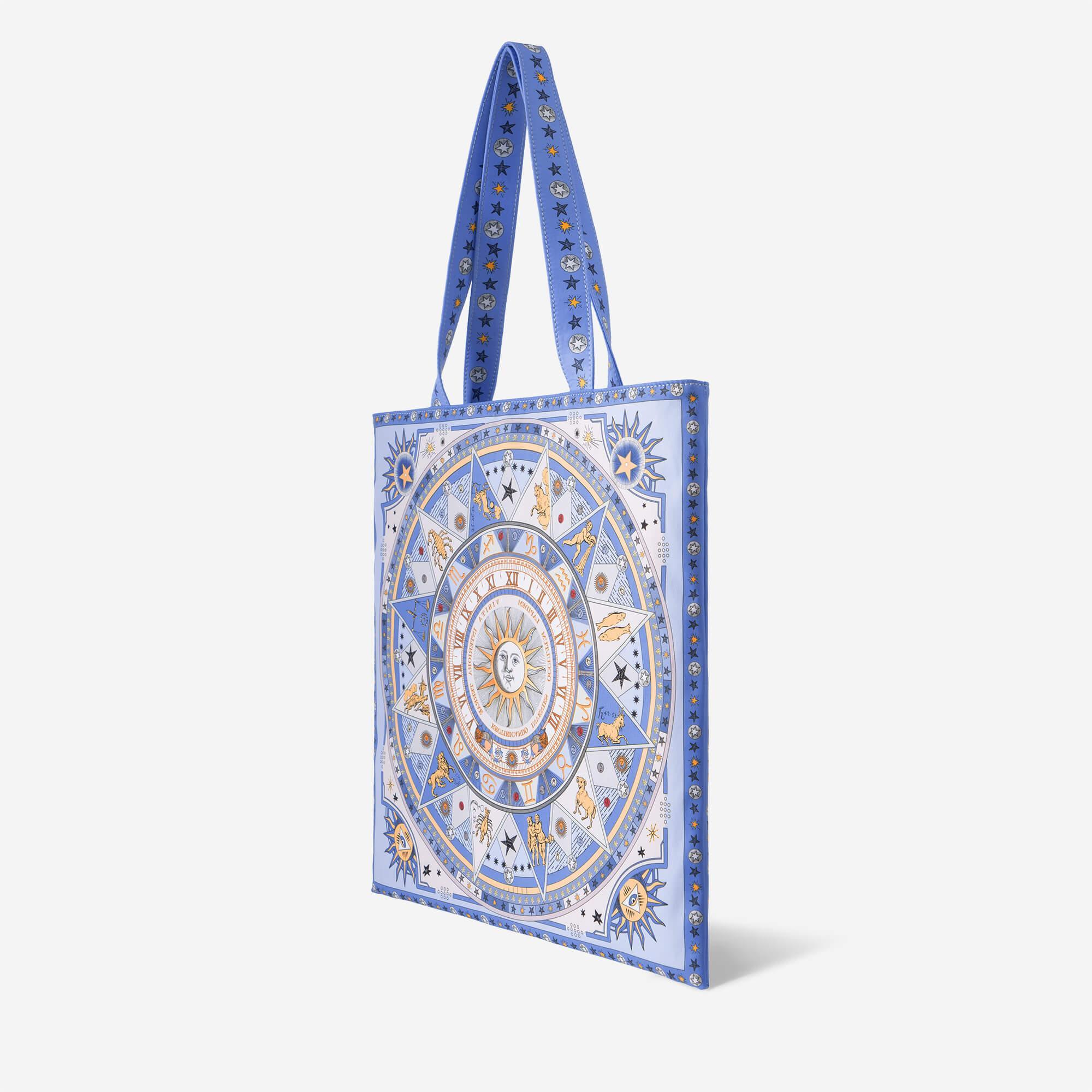 Blue tote bag with celestial zodiac print, star-patterned straps, and sun motif design