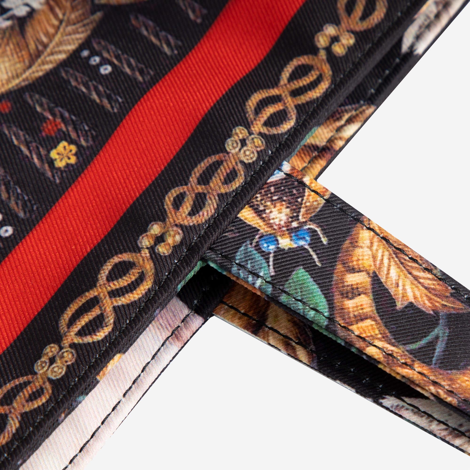 Floral and chain print backpack strap with red stripe, detailed stitching, and nature-inspired design
