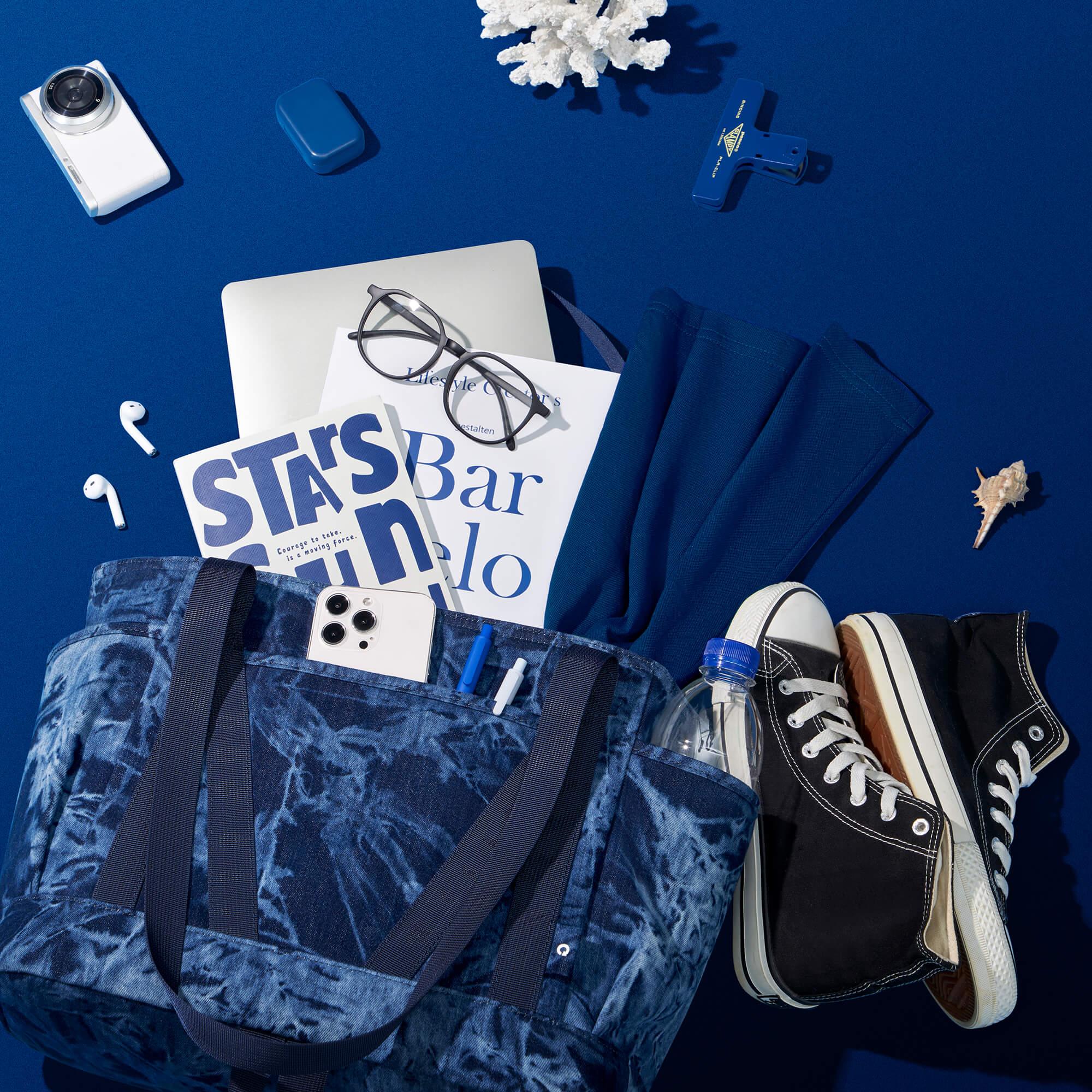Blue tie-dye tote bag with laptop, phone, sneakers, and accessories on navy background