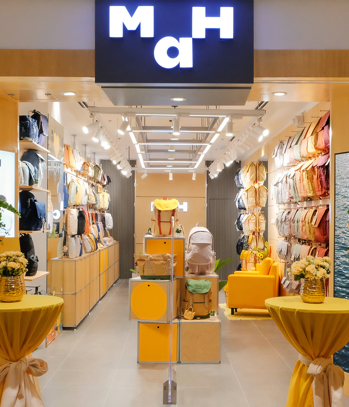 Modern retail store displaying colorful backpacks, bags, and accessories with bright lighting and yellow decor