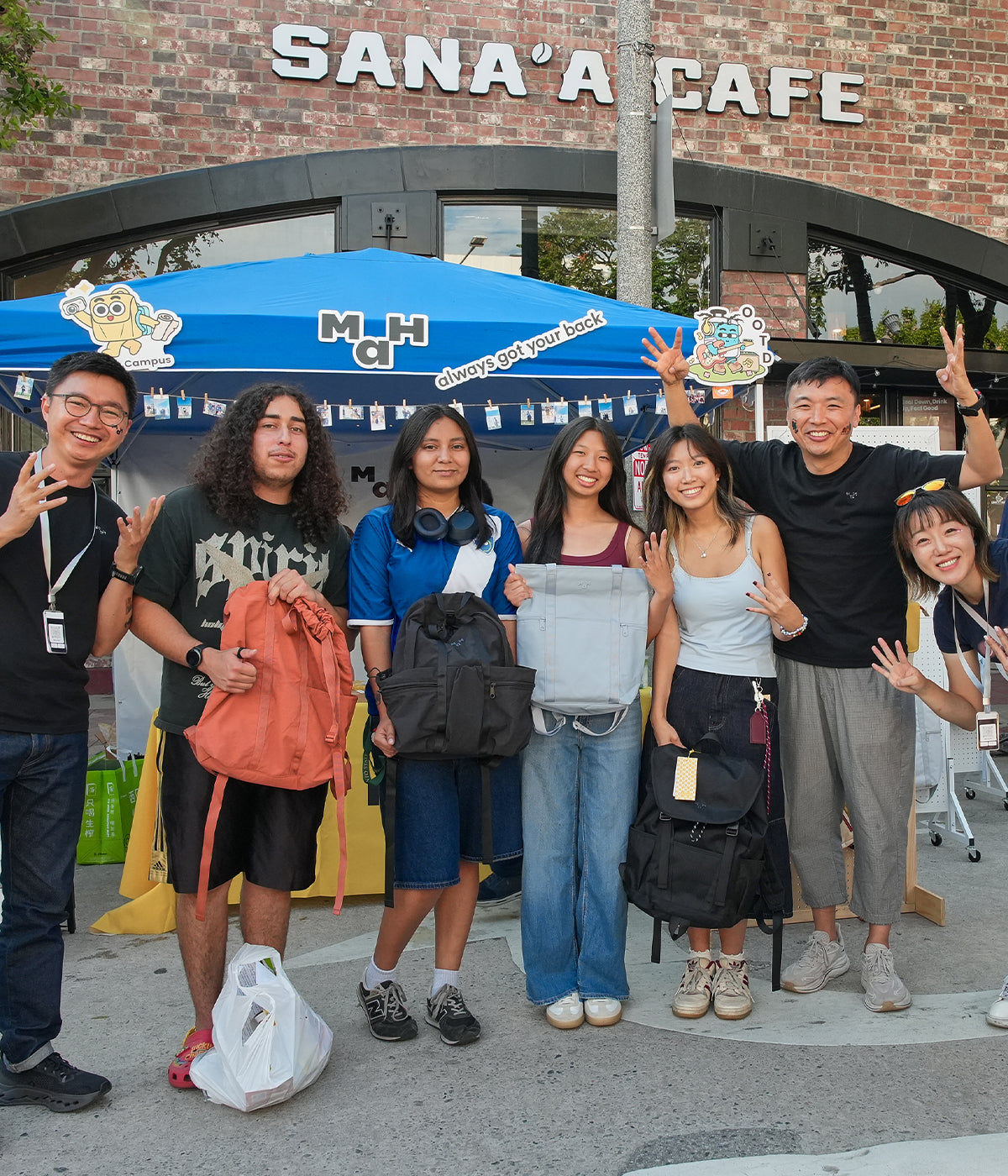 Students and staff posing with MaH backpacks at a UCLA Welcome Week event booth.