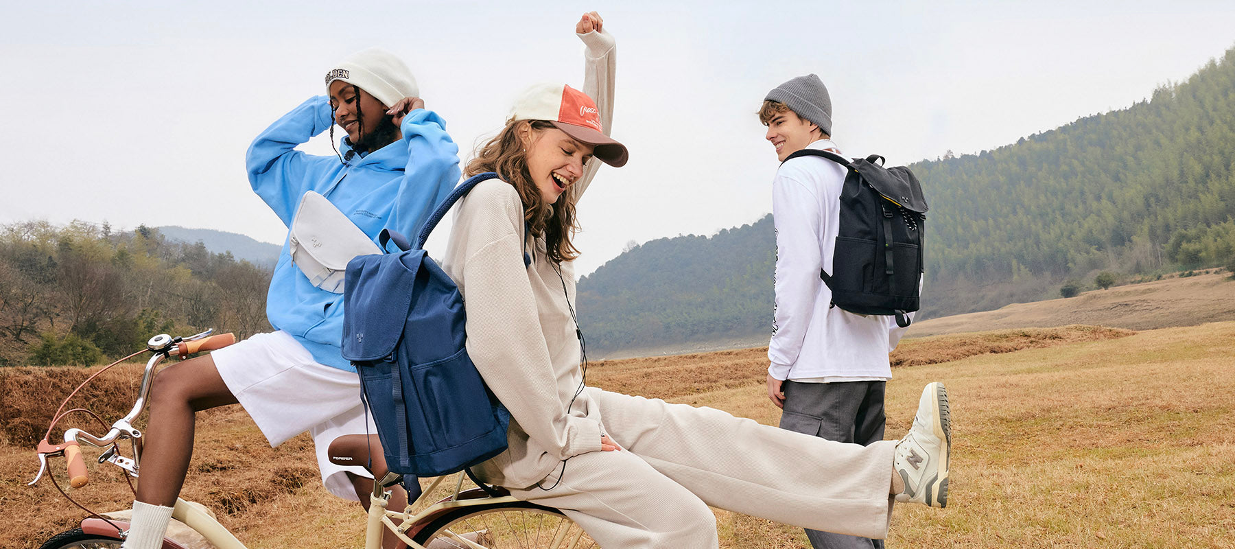 Young friends with backpacks and crossbody bags enjoying a bike ride in a scenic field, perfect for everyday adventures.
