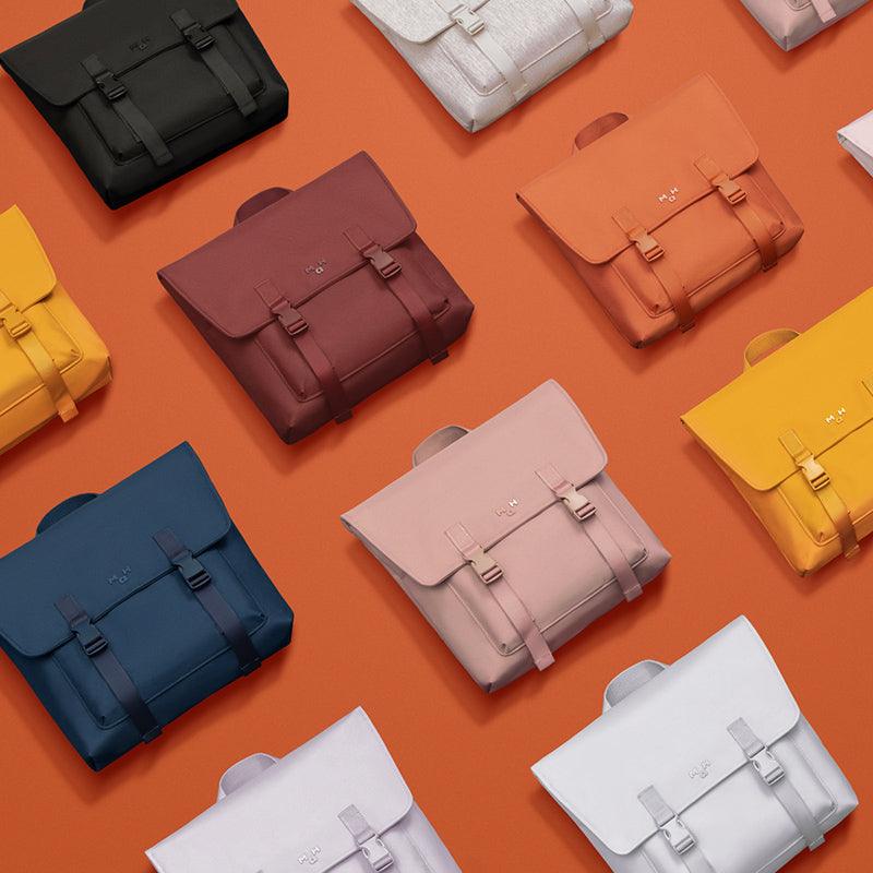 Colorful minimalist backpacks with flap closures on orange background, ideal for everyday use and travel