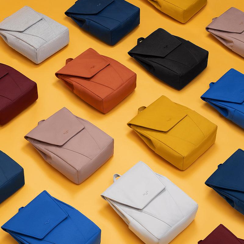 Colorful minimalist backpacks in assorted hues on yellow background, ideal for everyday carry and travel