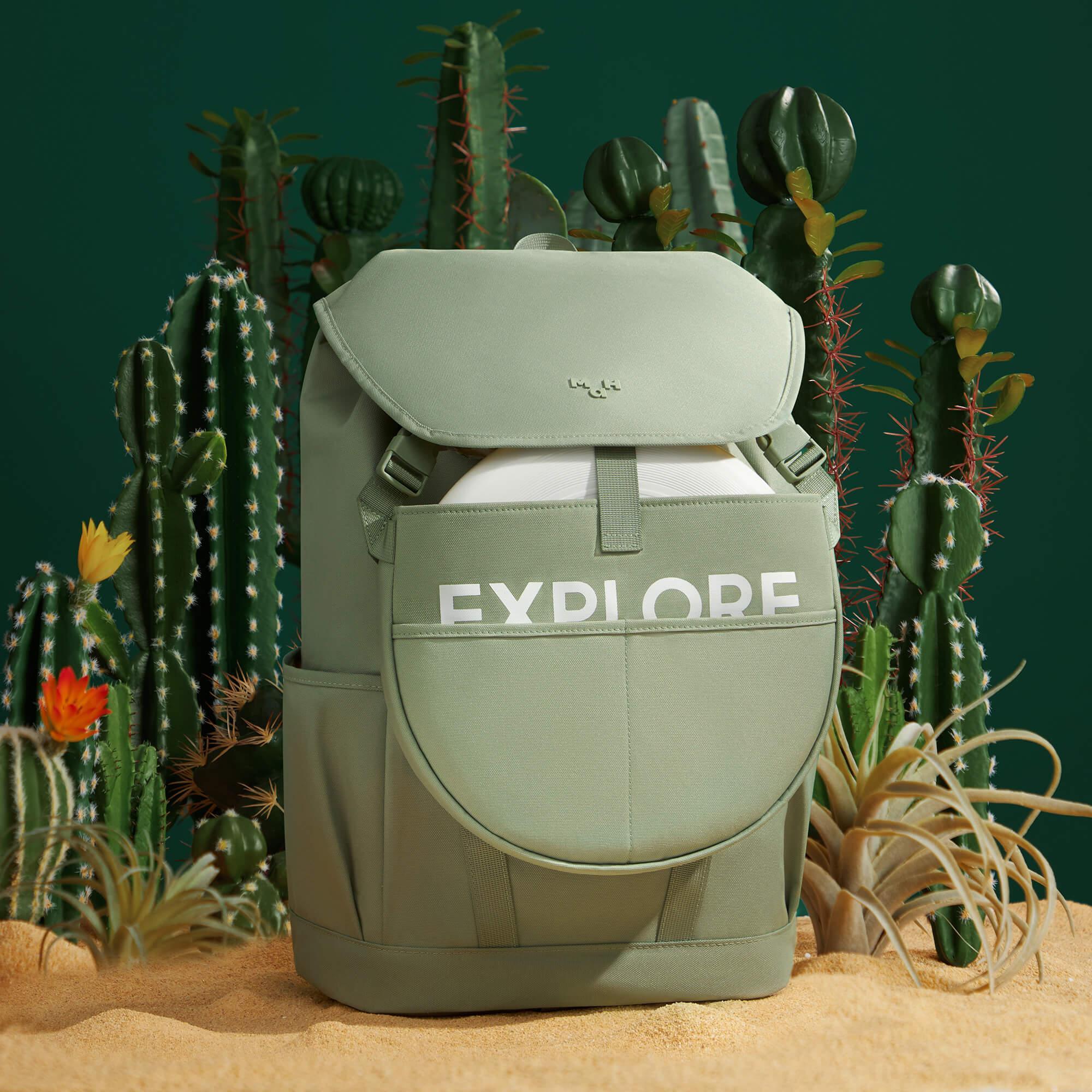 Sage green backpack with 'EXPLORE' print, set among cacti and desert sand for adventure travel