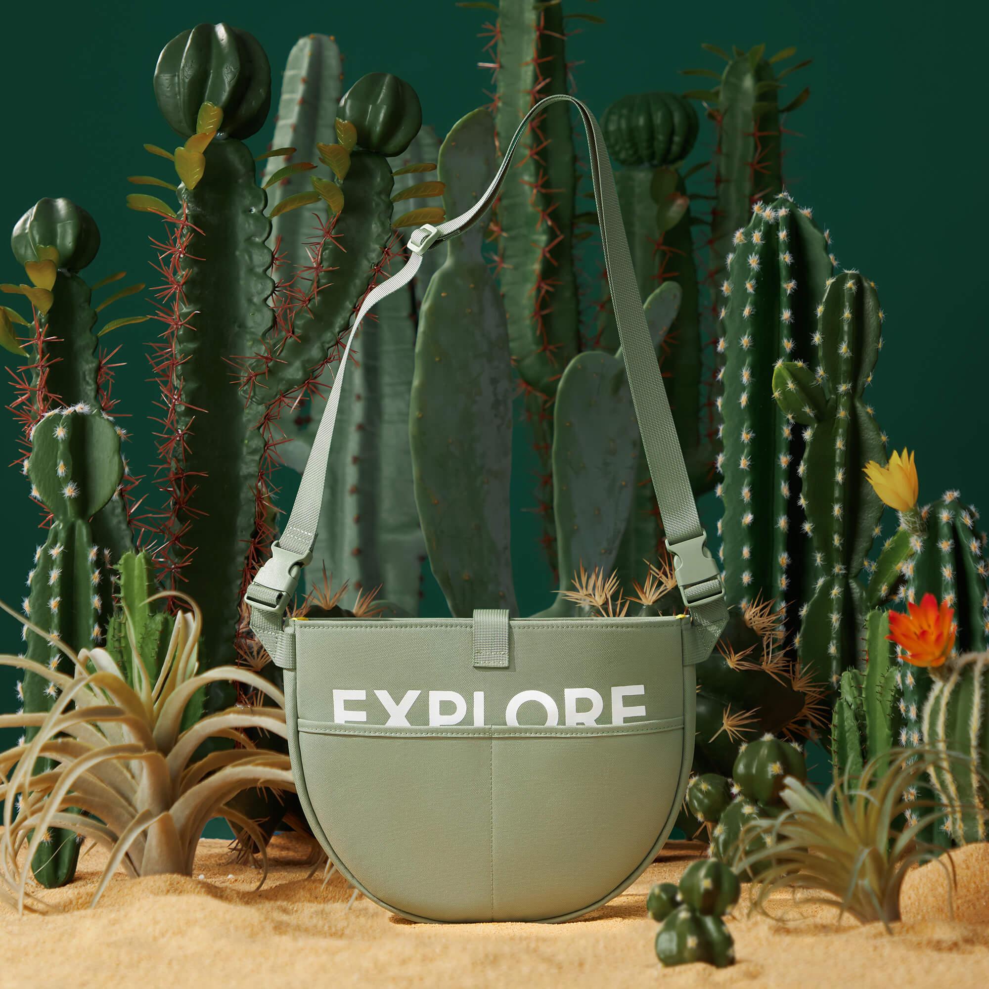 Green 'EXPLORE' crossbody bag with adjustable strap, styled in desert cactus scene for adventure travel.