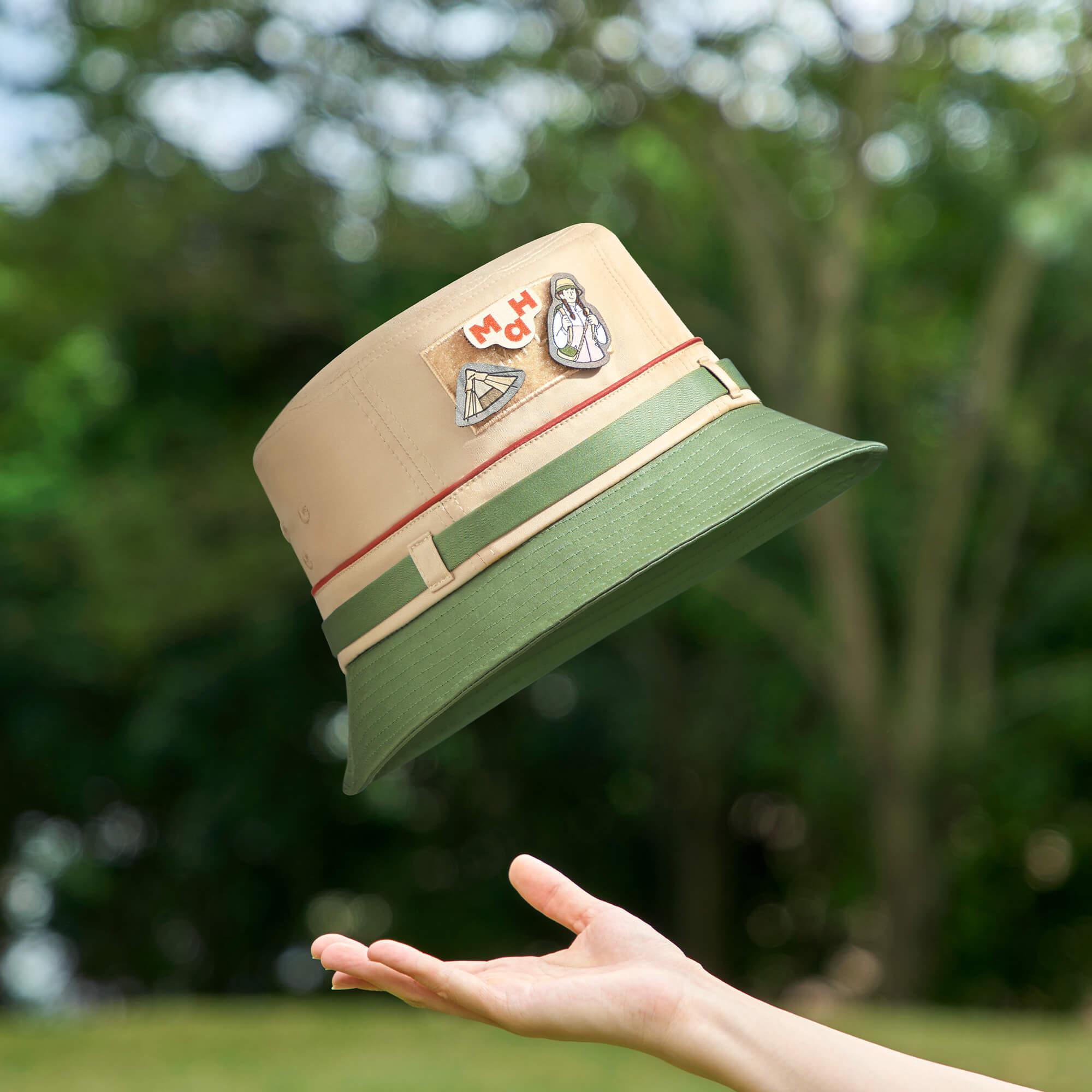 Beige and green bucket hat with patches, tossed outdoors for summer adventures