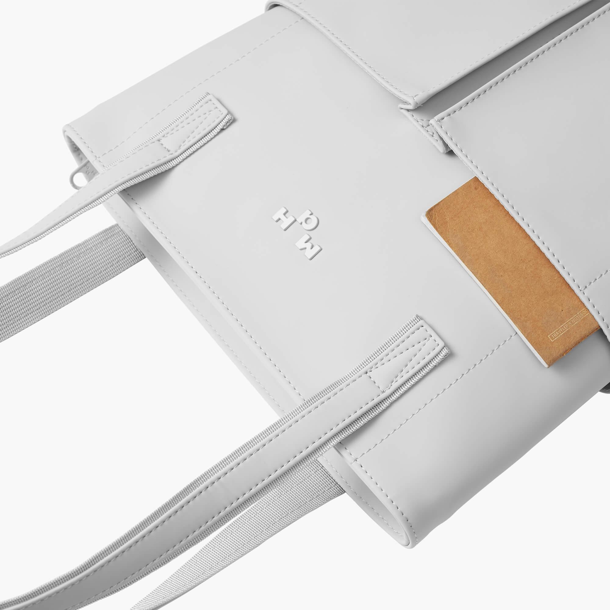 Light gray minimalist backpack with embossed logo, adjustable straps, and tan leather accent patch