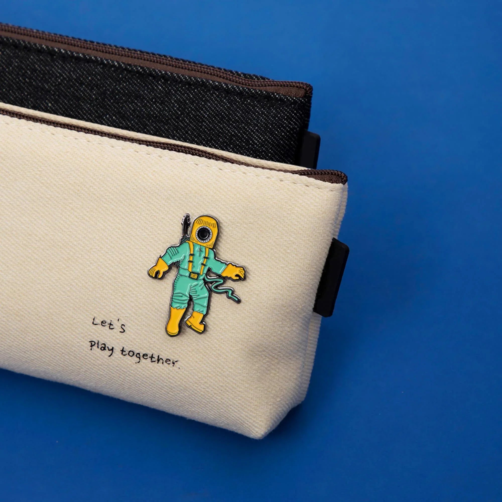 Cream canvas pouch with astronaut pin and 'Let's play together' text, blue background