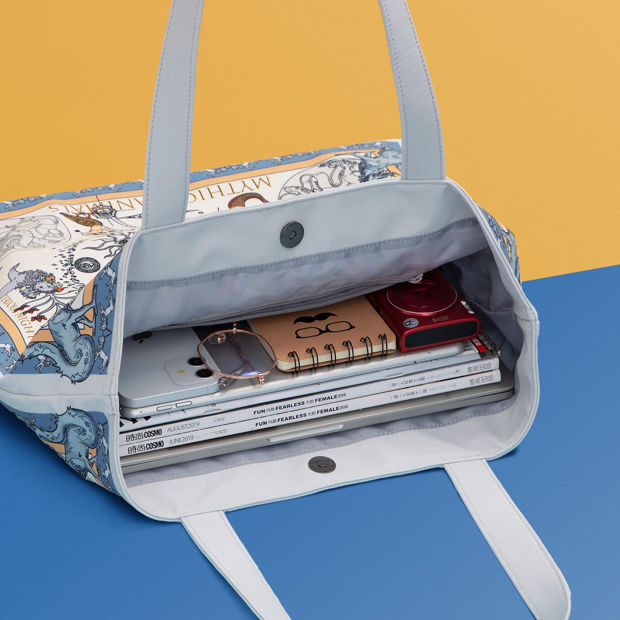 Stylish tote bag with mythical animal print, holding laptop, notebooks, and camera on colorful background