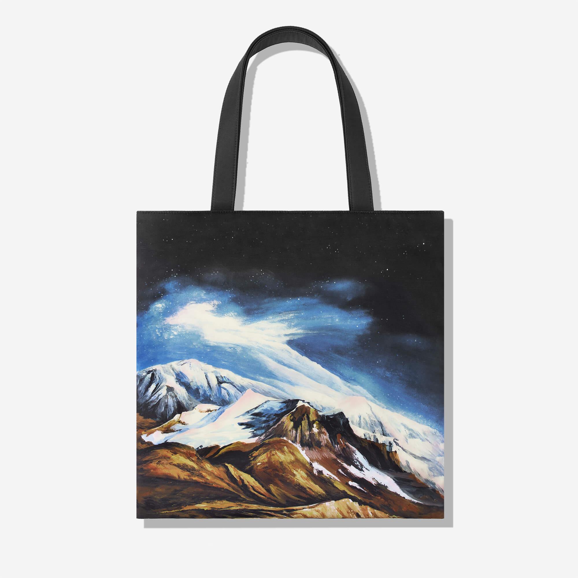 Tote bag with snowy mountain landscape under starry night sky, black handles, artistic print