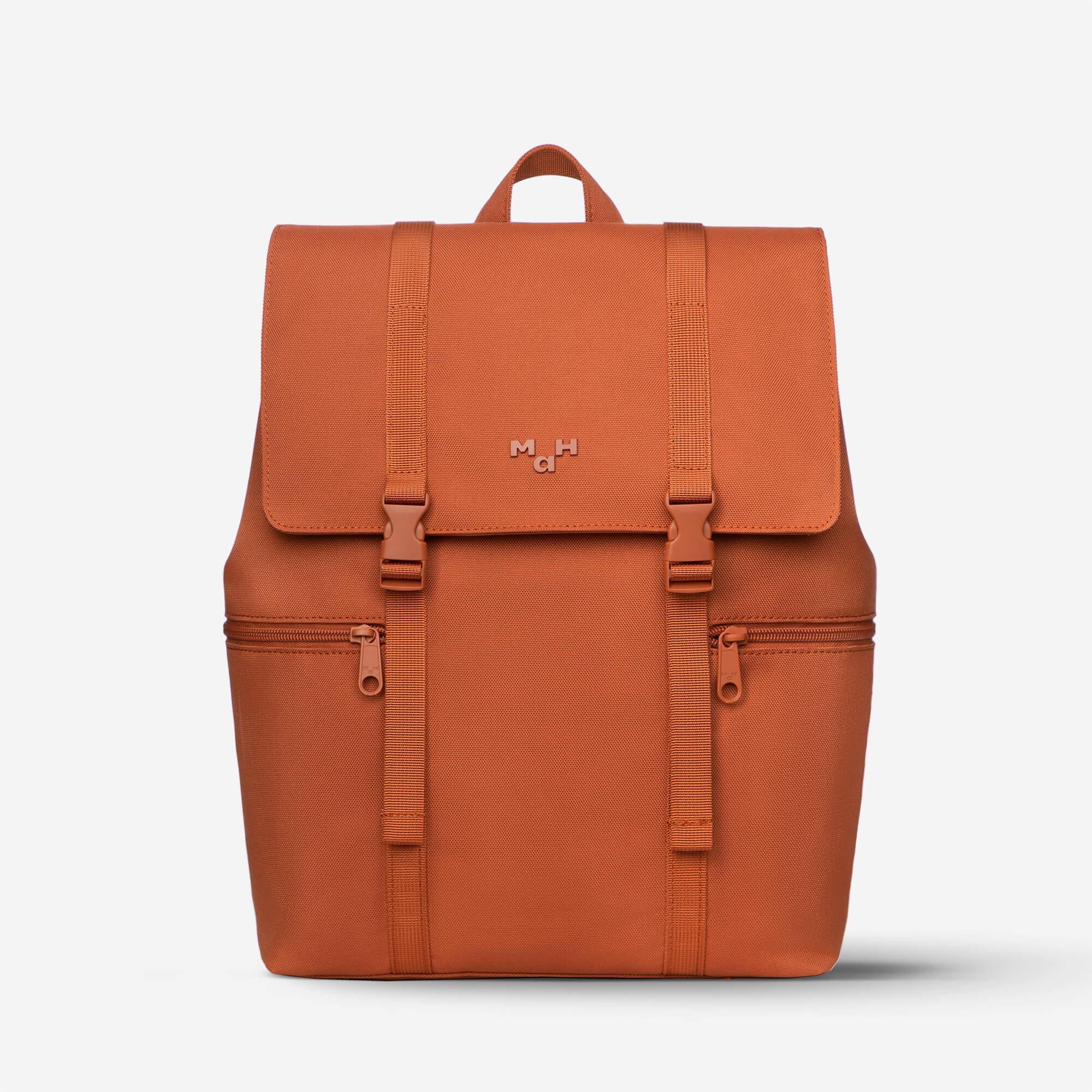 Rust orange backpack with front flap, buckles, and dual zippers, featuring minimalist design and brand logo.