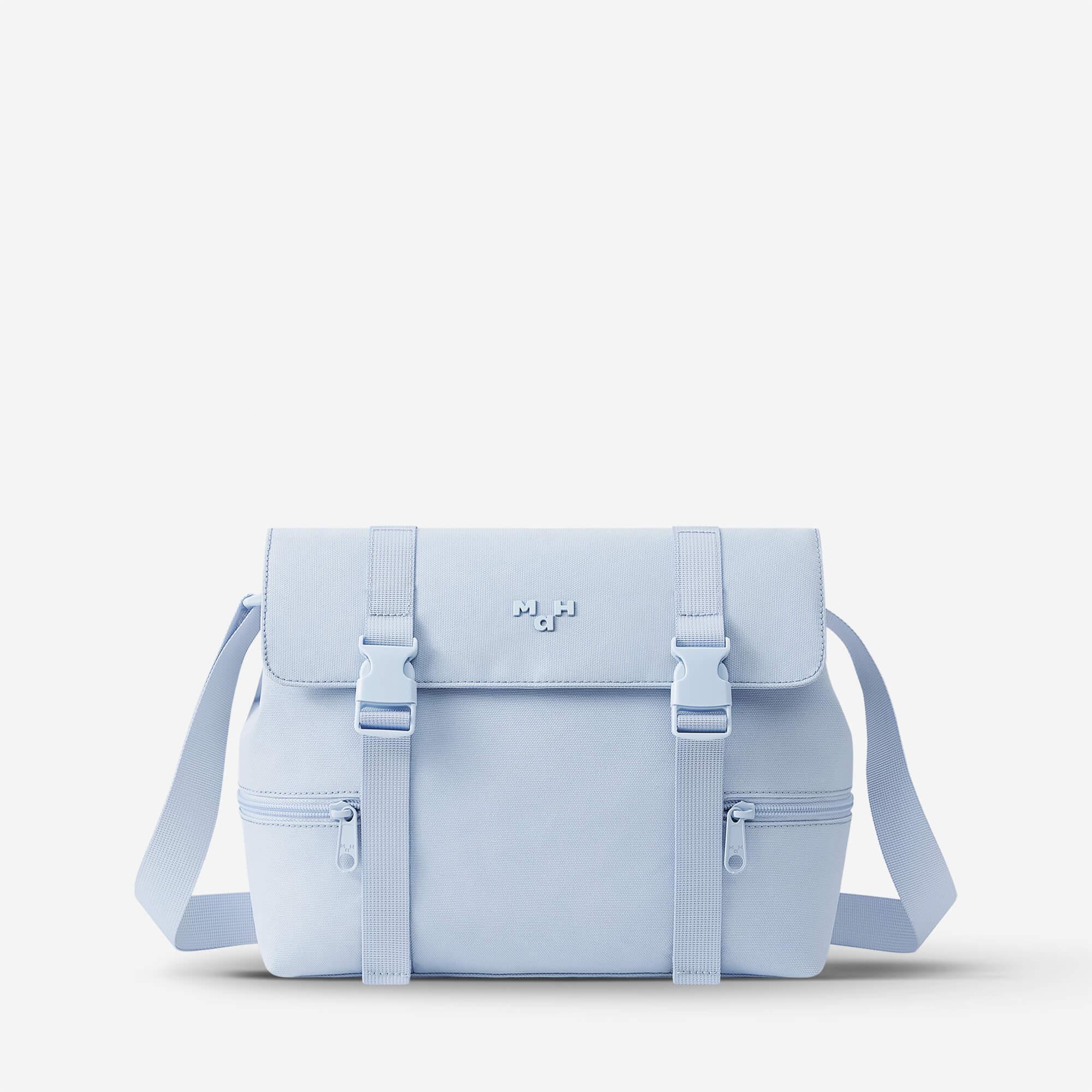 Light blue canvas satchel bag with adjustable straps and front zip pockets, minimalist design