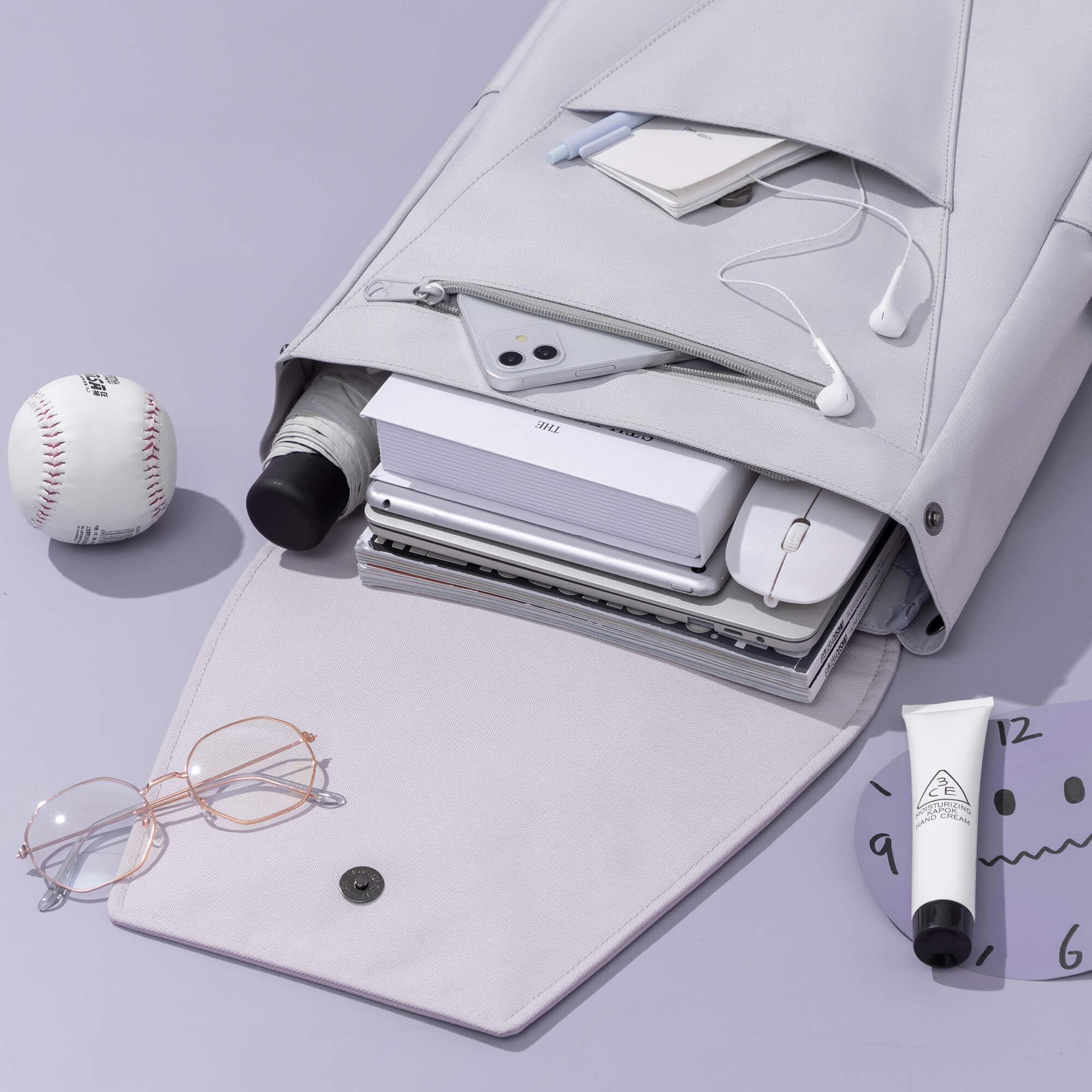 Light gray backpack filled with laptop, books, phone, earbuds, and accessories for school or daily use