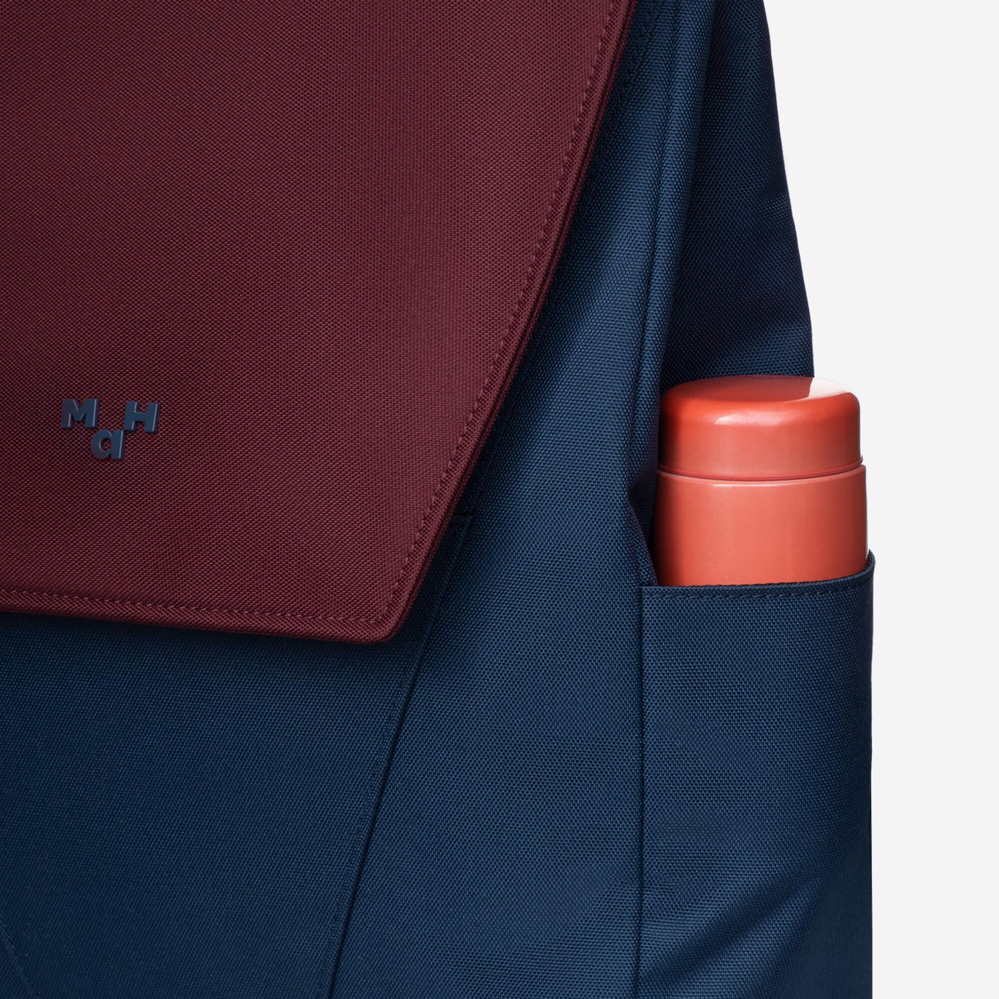 Maroon and navy backpack with side pocket holding orange water bottle, featuring subtle logo detail