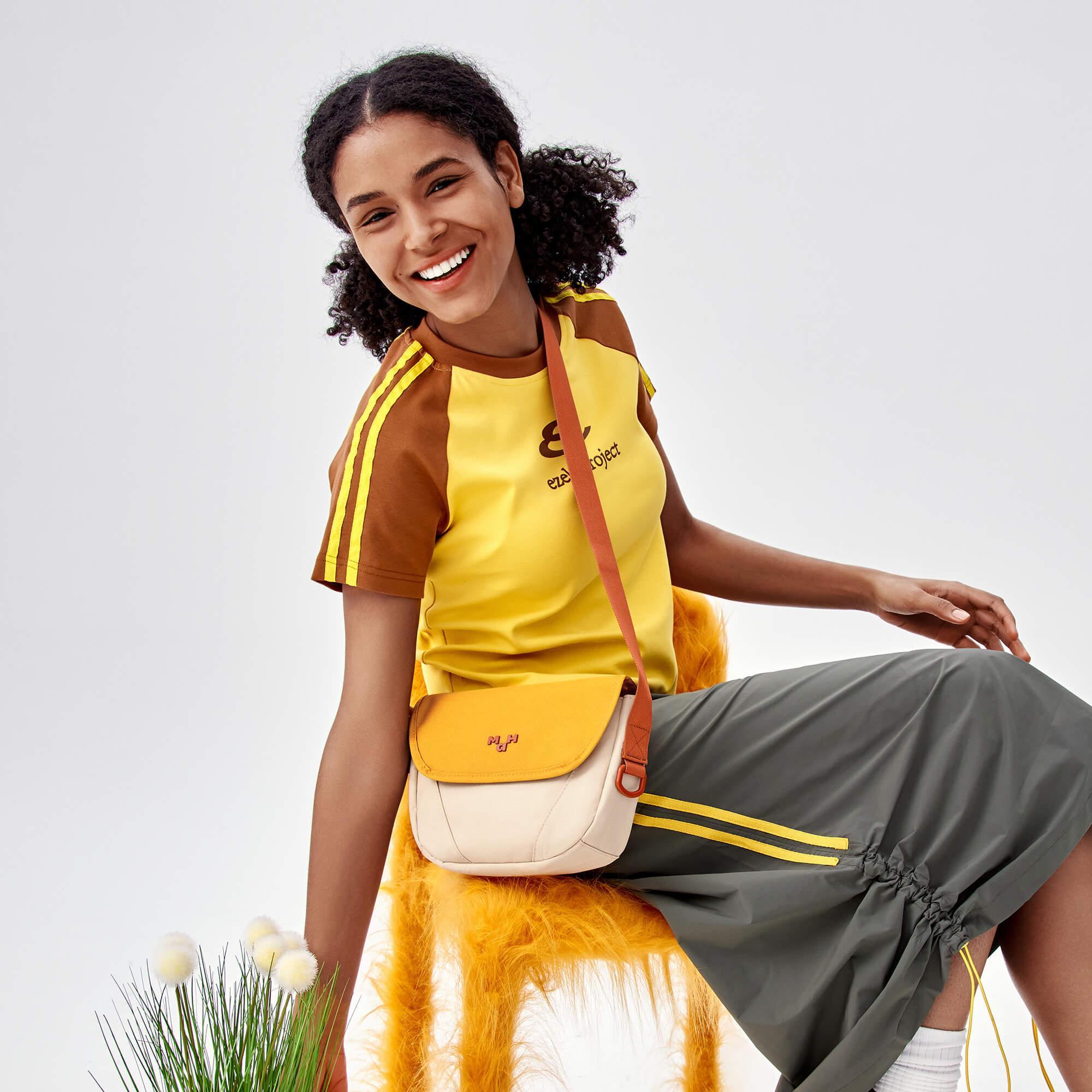 Stylish yellow and cream crossbody bag with adjustable strap, worn by smiling woman in casual outfit