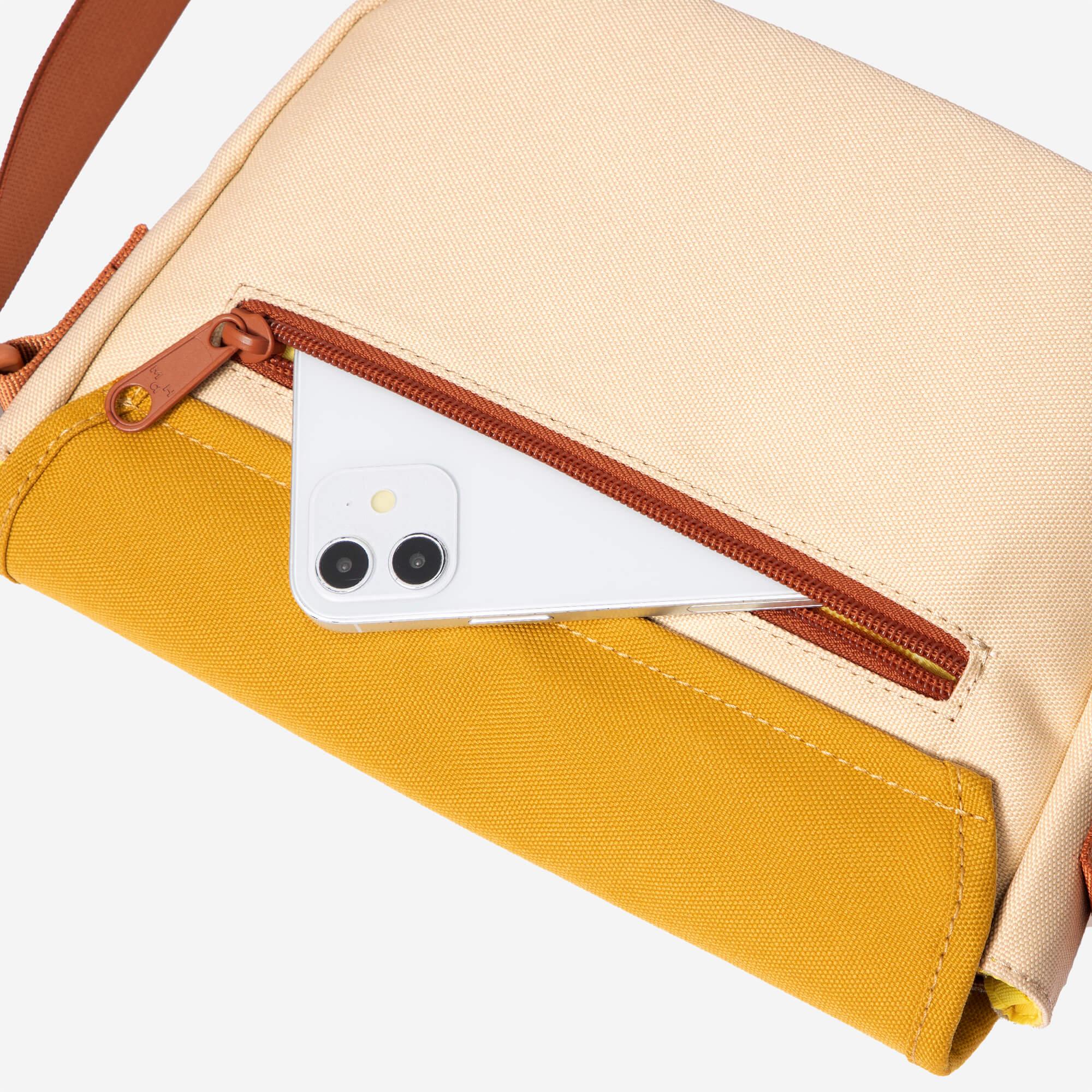 Beige and mustard canvas crossbody bag with brown zipper, holding a white smartphone in front pocket