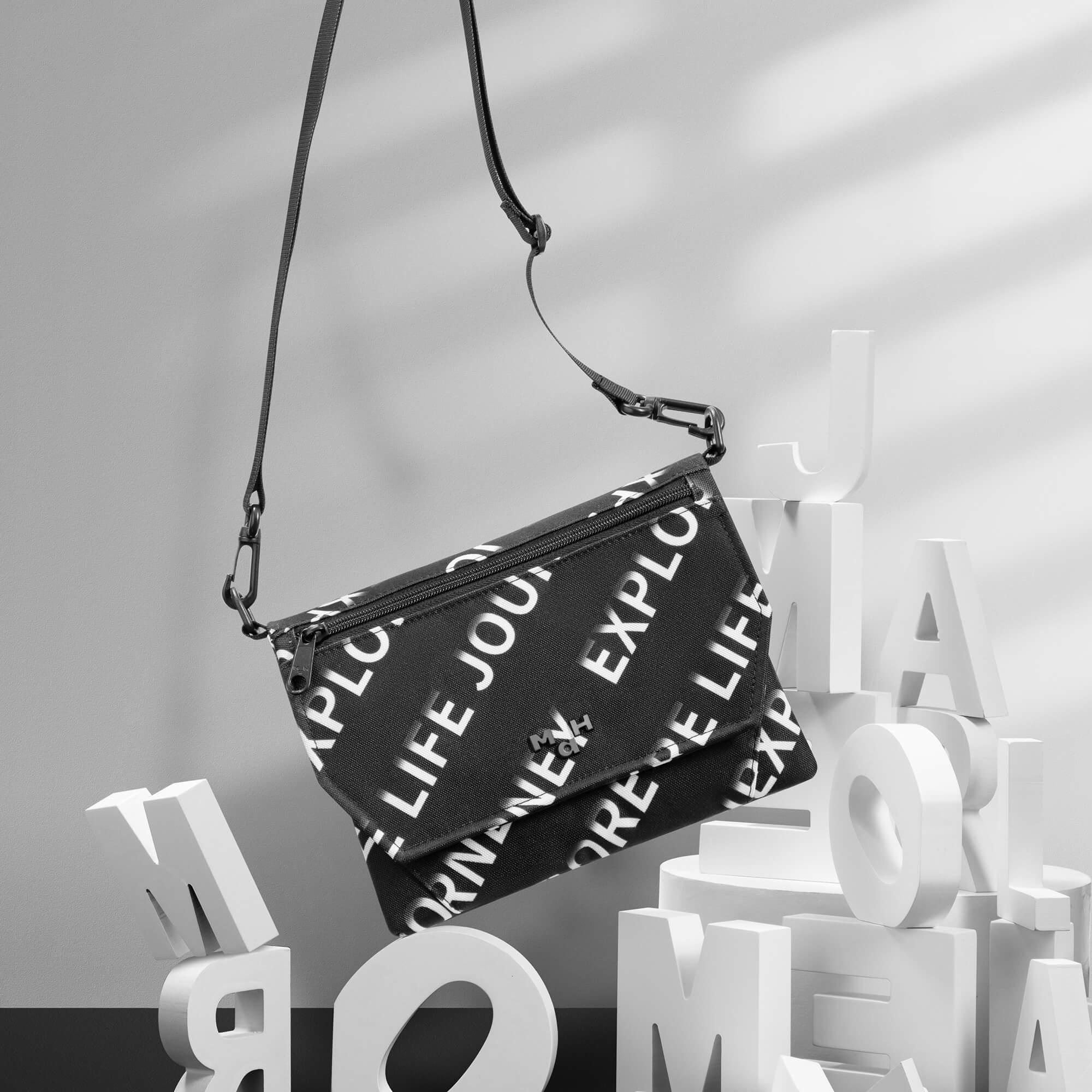 Black crossbody bag with bold white text print, adjustable strap, styled with large white letters for modern lifestyle look.