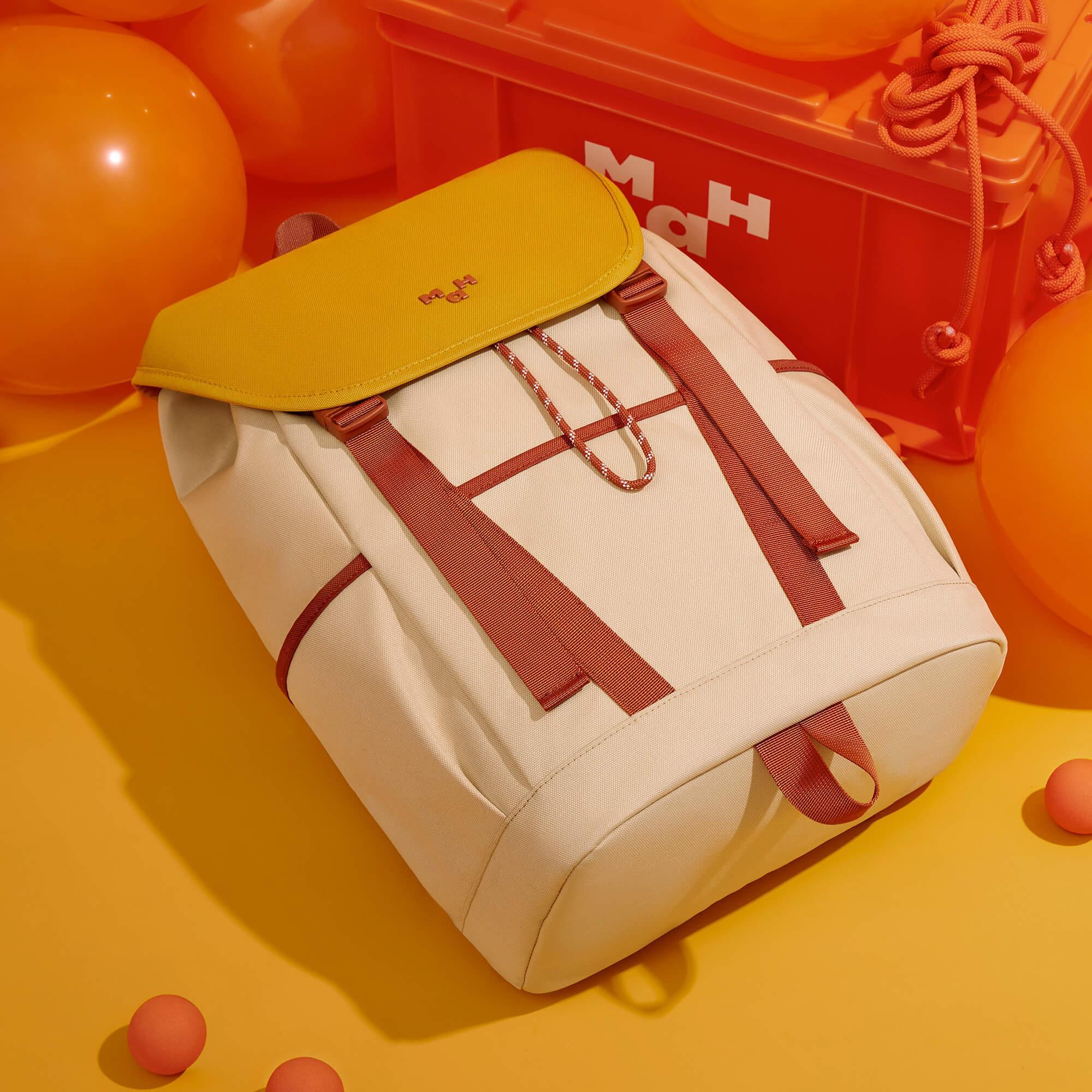 Cream canvas backpack with mustard flap and rust straps, styled with orange balloons and storage crate