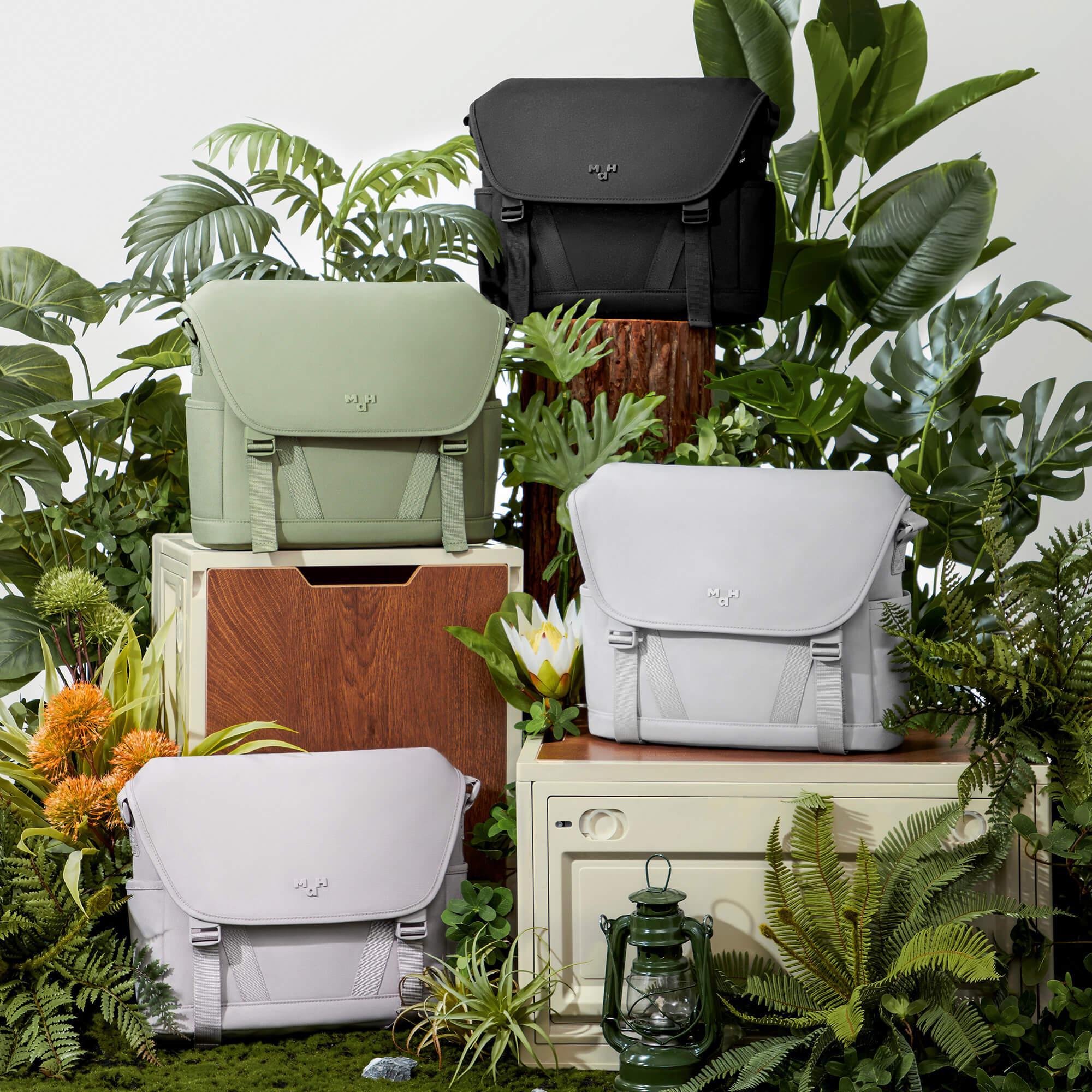 Stylish messenger bags in black, sage, white, and lavender displayed with lush green plants and vintage decor