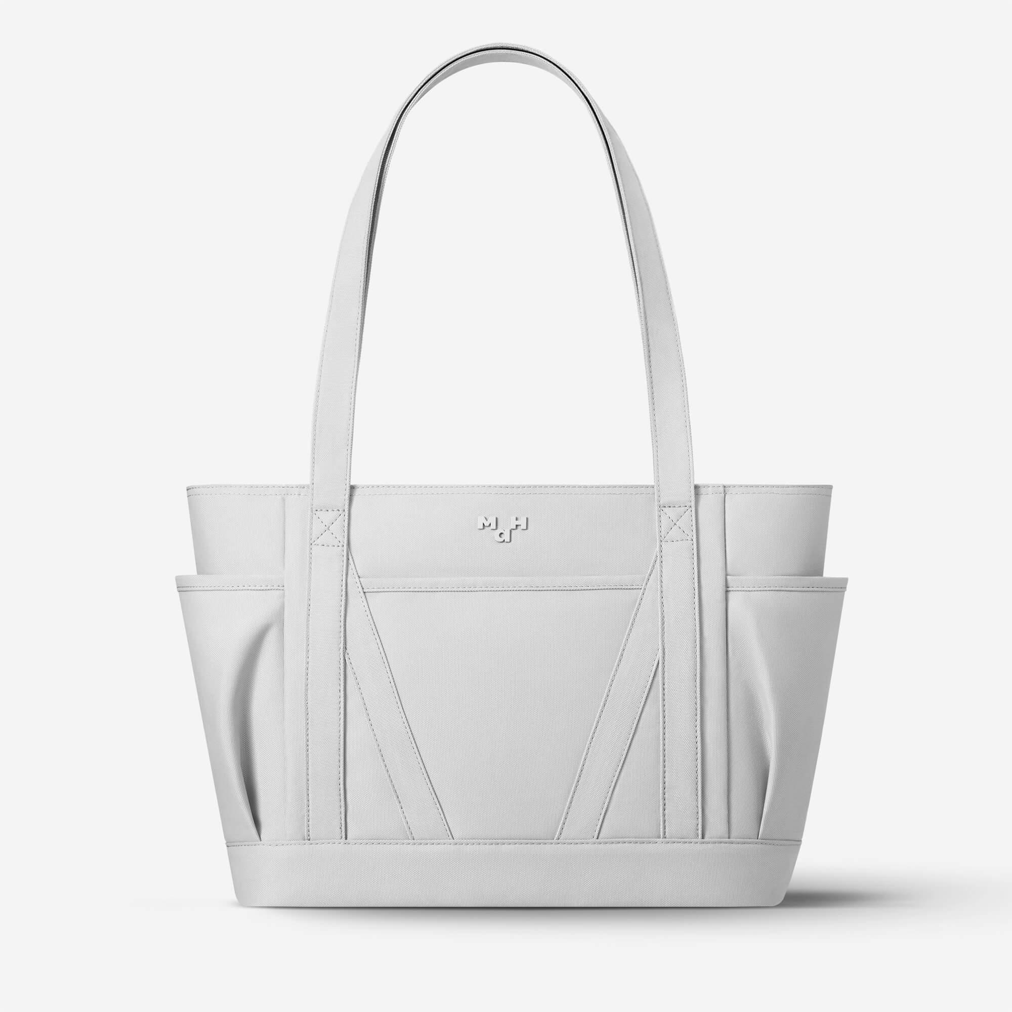 Light gray tote bag with structured design, side pockets, and minimalist logo, ideal for everyday carry and lifestyle use.