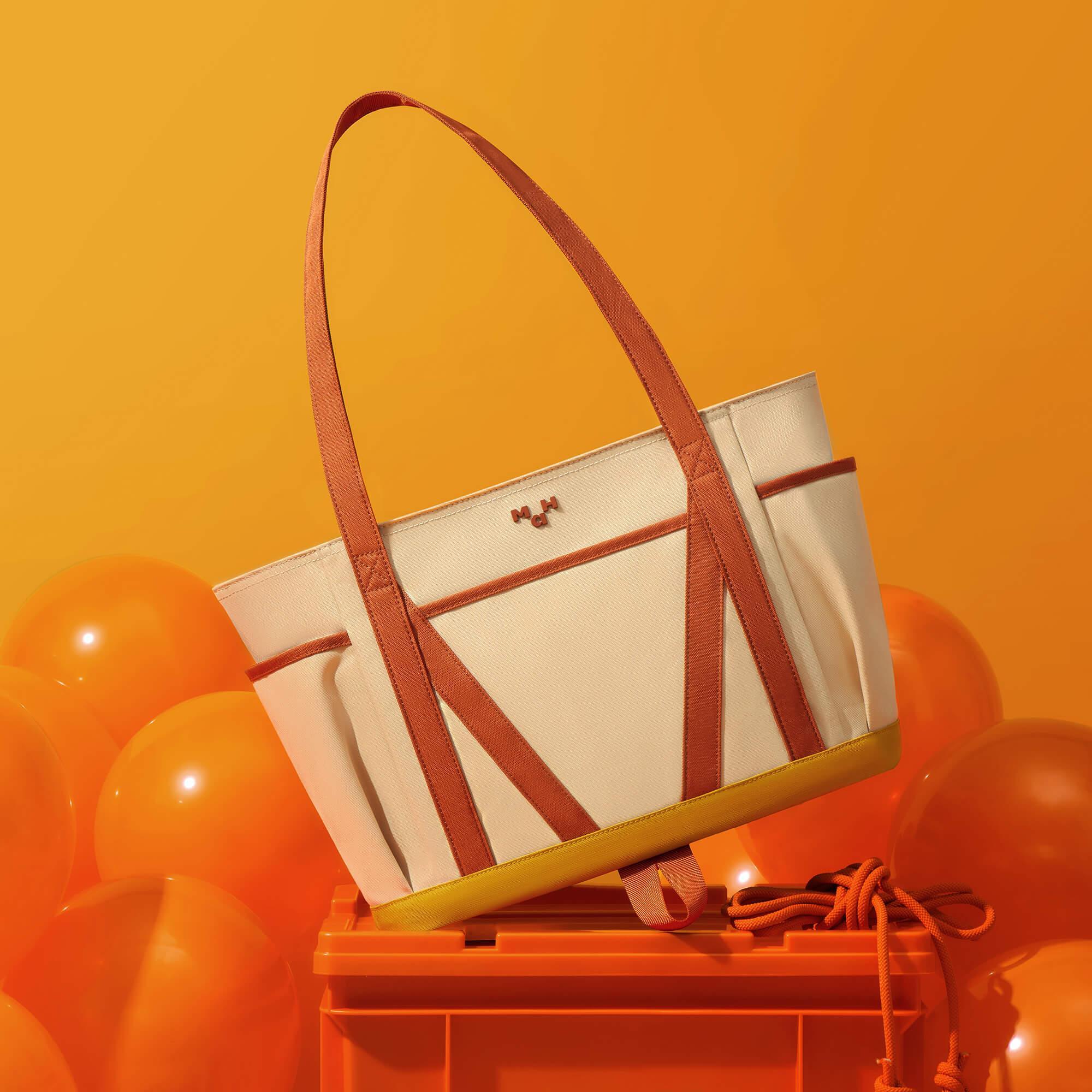 Cream canvas tote bag with rust straps and yellow base, styled with orange balloons on crate
