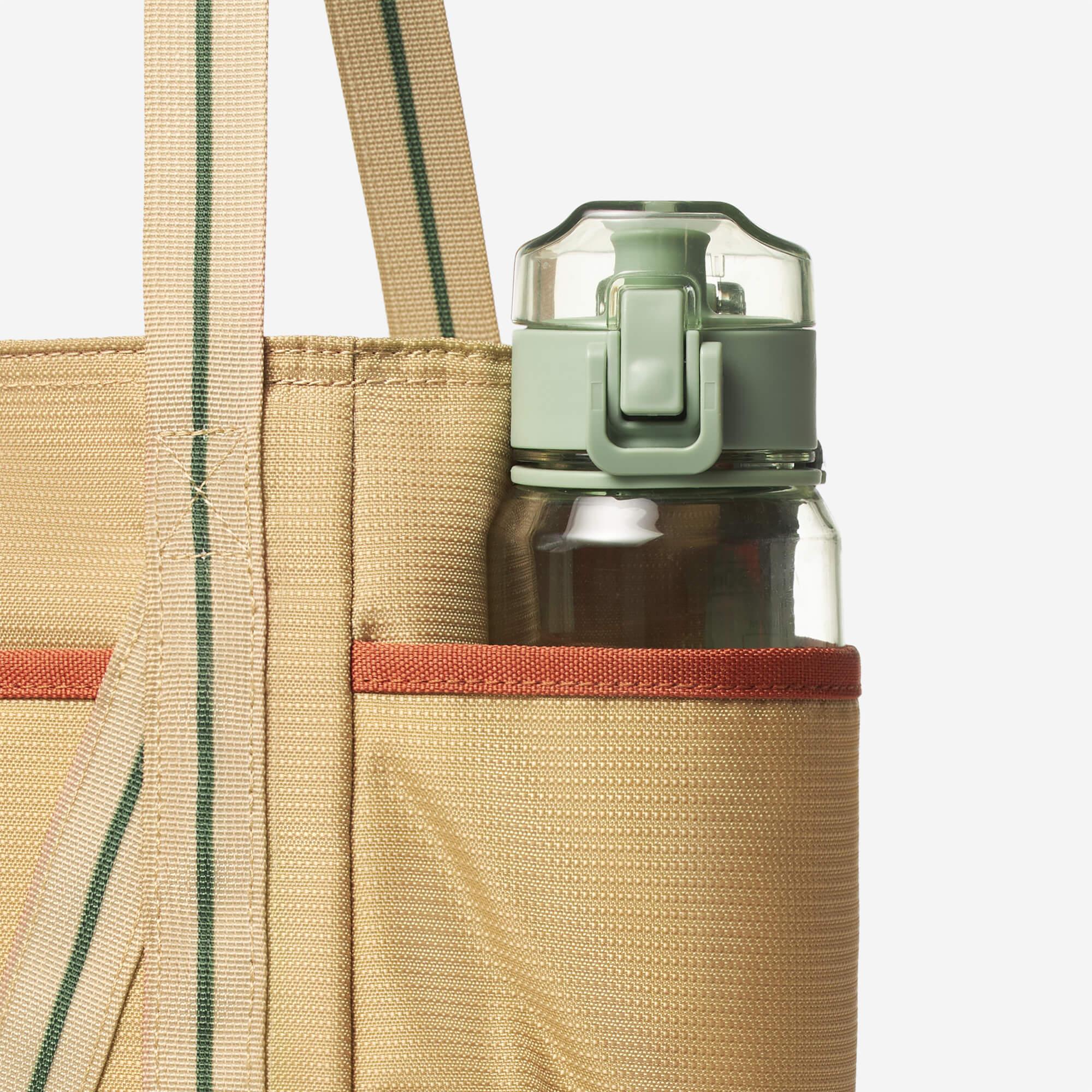 Beige tote bag with green stripe and side pocket holding a water bottle, ideal for daily use and travel.