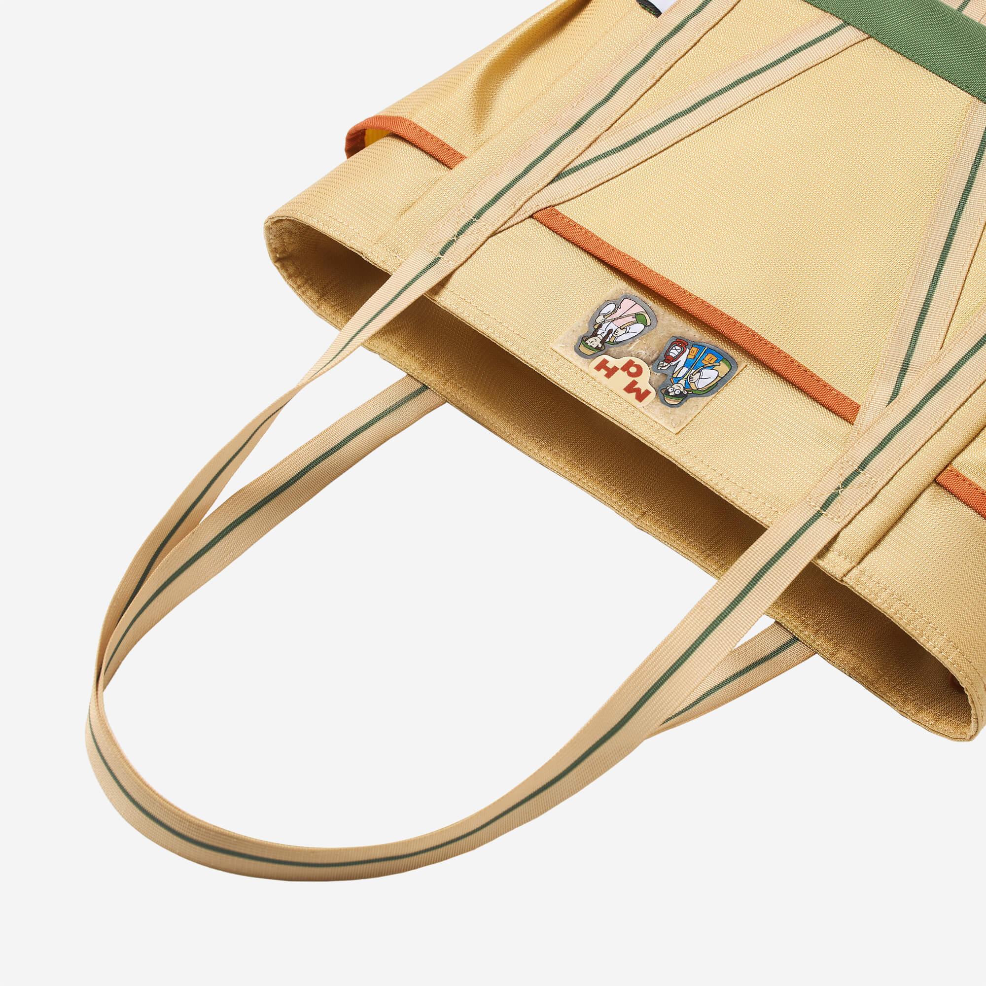 Beige tote bag with green stripes, orange trim, and cartoon patch detail for everyday carry.