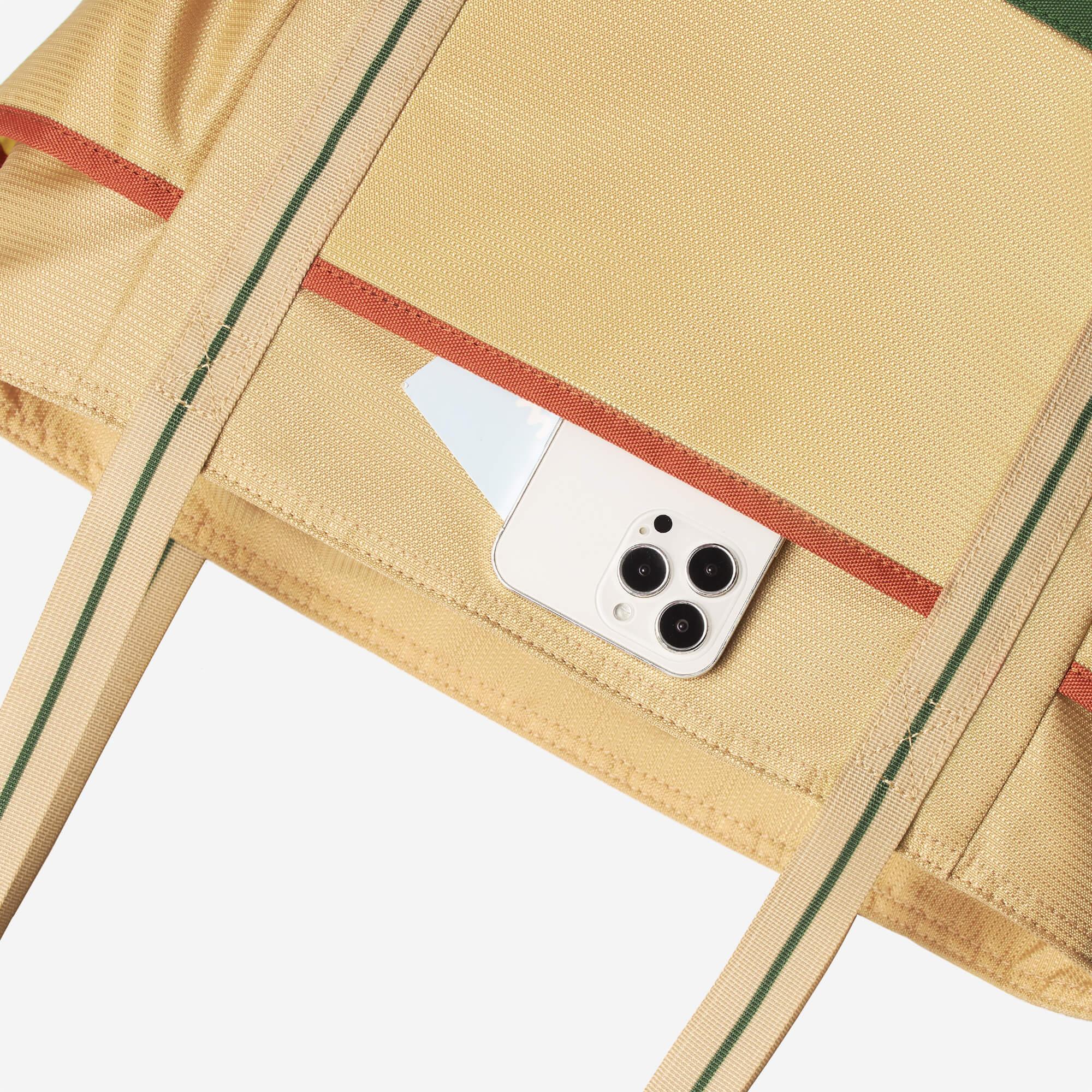 Beige tote bag with green and red stripes, holding a white smartphone in side pocket